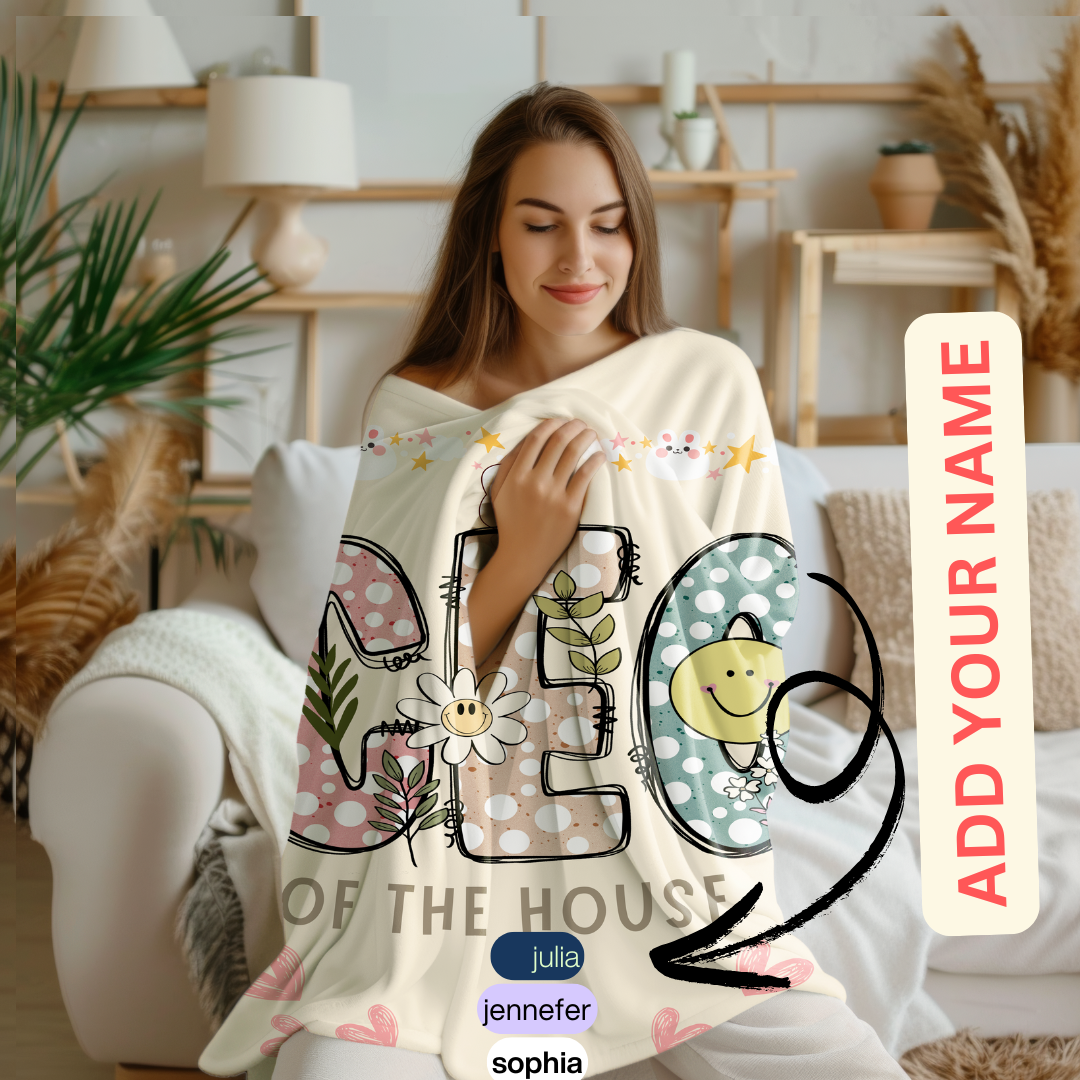 A woman wrapped in a cozy sherpa fleece blanket with a colorful 'CEO of the House' design featuring floral patterns and playful text. The blanket includes a customizable name option, showcasing examples like 'Julia,' 'Jennifer,' and 'Sophia.' Perfect for personalized gifts or home decor.