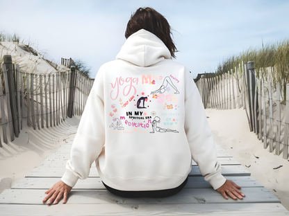 Back view of a white hoodie featuring colorful yoga-inspired designs and motivational text for mindfulness and meditation, displayed on a boardwalk by a beach.